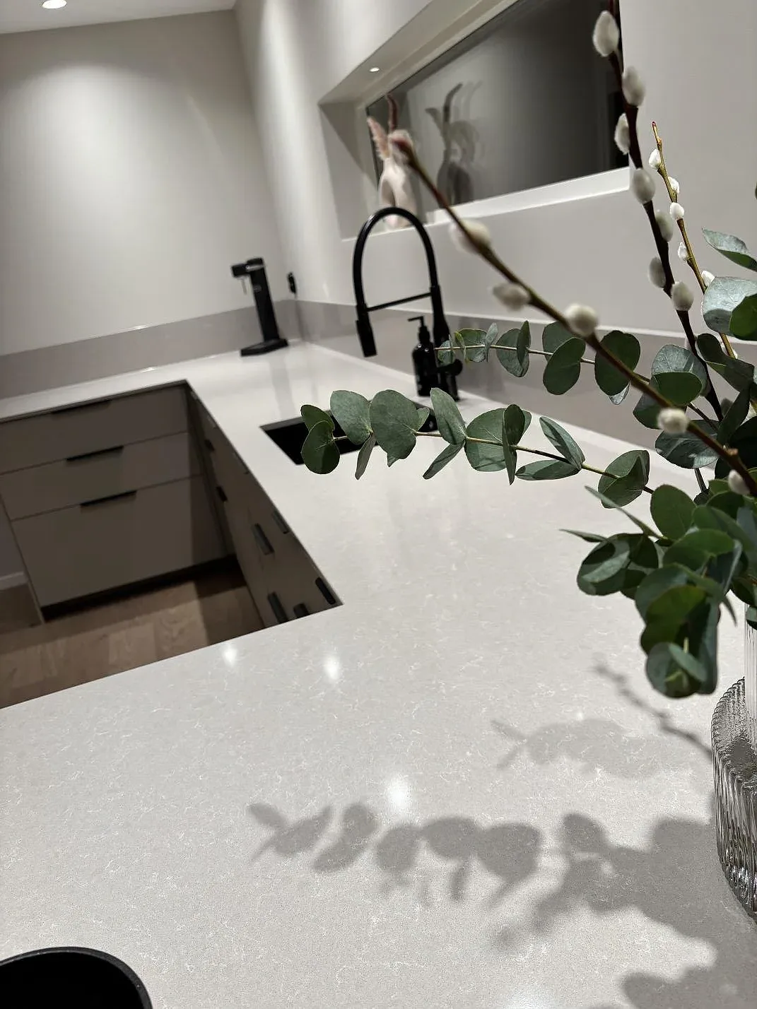Närbild på polerad Technistone Noble Ivory White i kvartskomposit med synlig struktur, svart blandare och diskzon i Gnosjö.