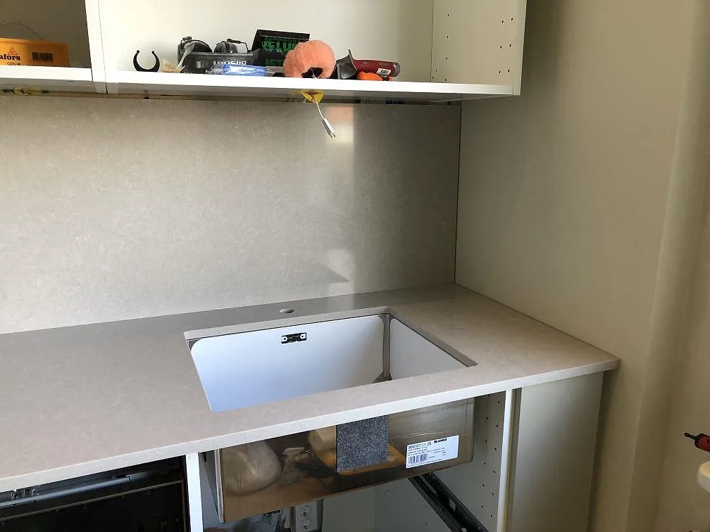 Hörnparti av köksbänkskiva i Technistone Noble Ivory White med underlimmad diskho och uppvikt stänkskydd i samma sten, Göteborg.