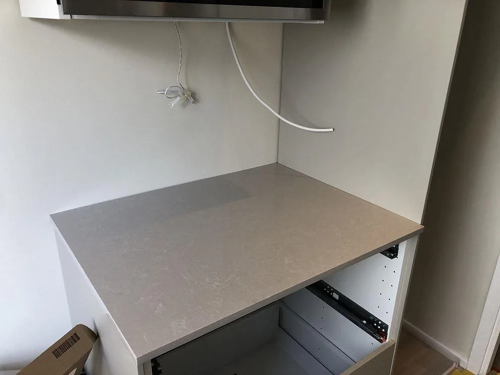 Stänkskydd och bänkskiva i Technistone Noble Ivory White med lugn ådringsfri yta i ett kök under montering, Göteborg.