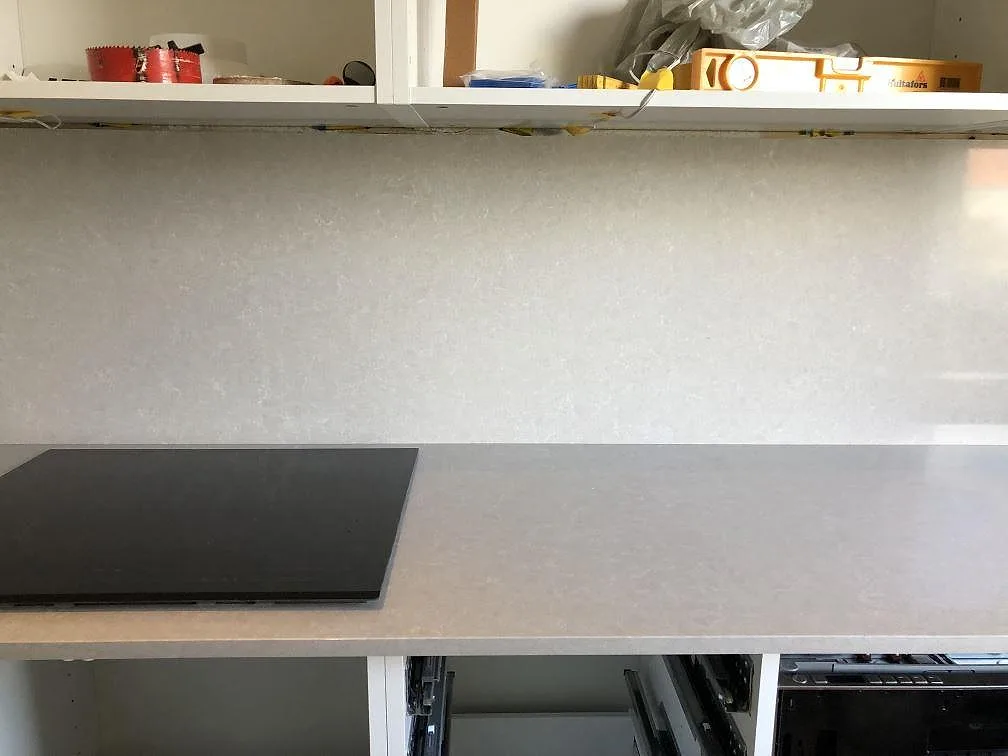 Köksbänkskiva i varmvit Technistone Noble Ivory White med stänkskydd och induktionshäll, fotograferad under montering i Göteborg.