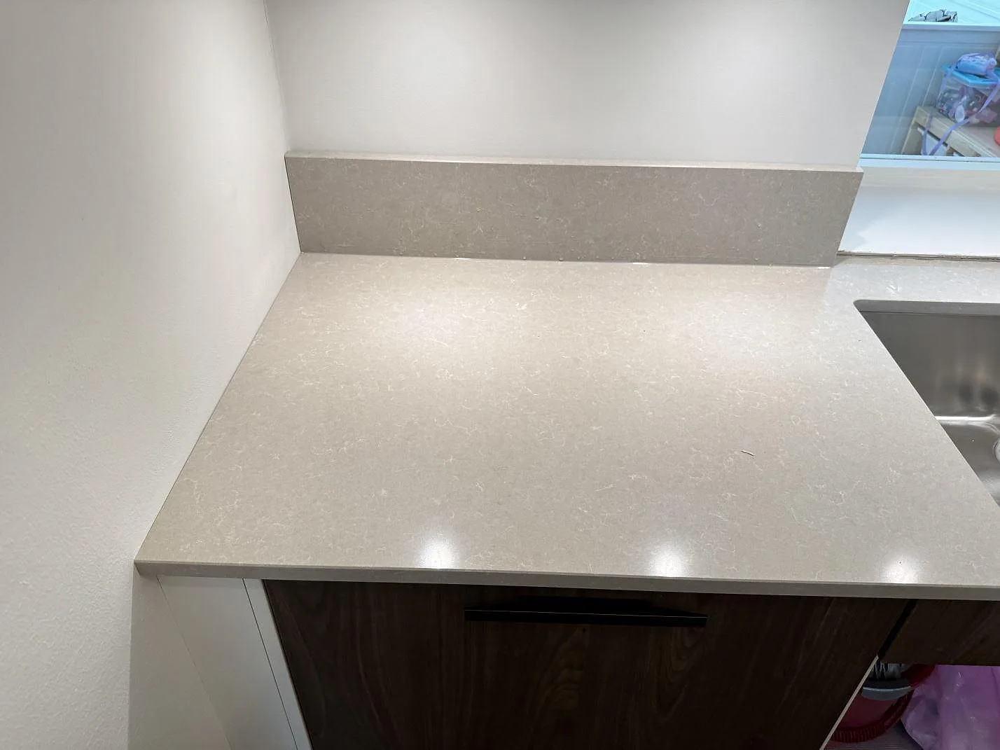 Närbild av polerad kvartskomposit, Technistone Noble Ivory White, som köksbänkskiva med uppvikt stänkkant intill diskhon i Göteborg.