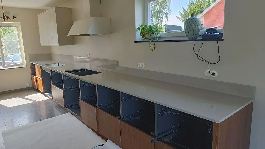 Köksbänkskiva i Technistone Noble Ivory White, polerad kvartskomposit, med stänkskydd och hälluttag i ett kök i Göteborg.