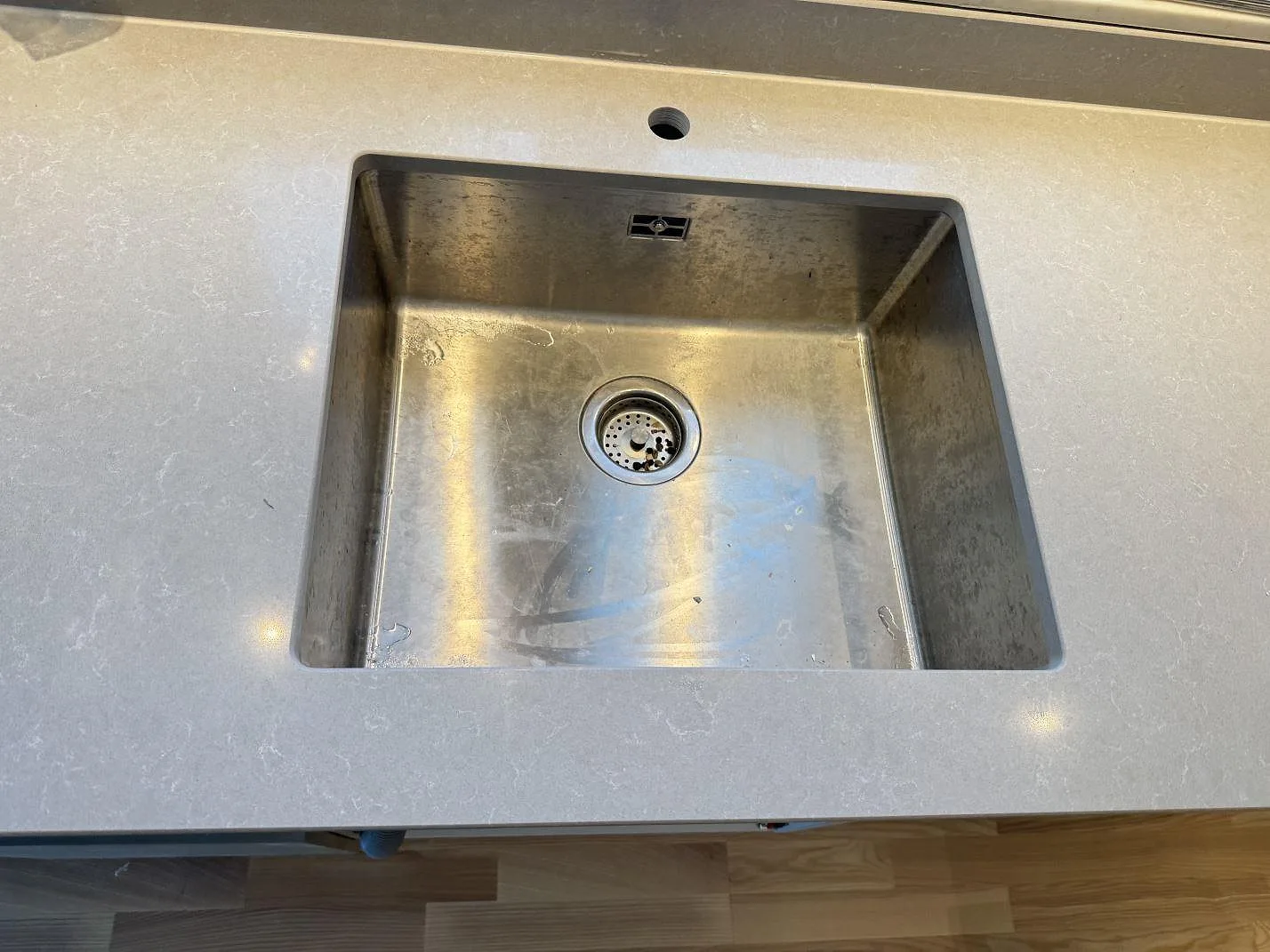 Rostfri diskho i en polerad kompositbänkskiva av Technistone Noble Ivory White, med runt blandarhål i köket i Göteborg.