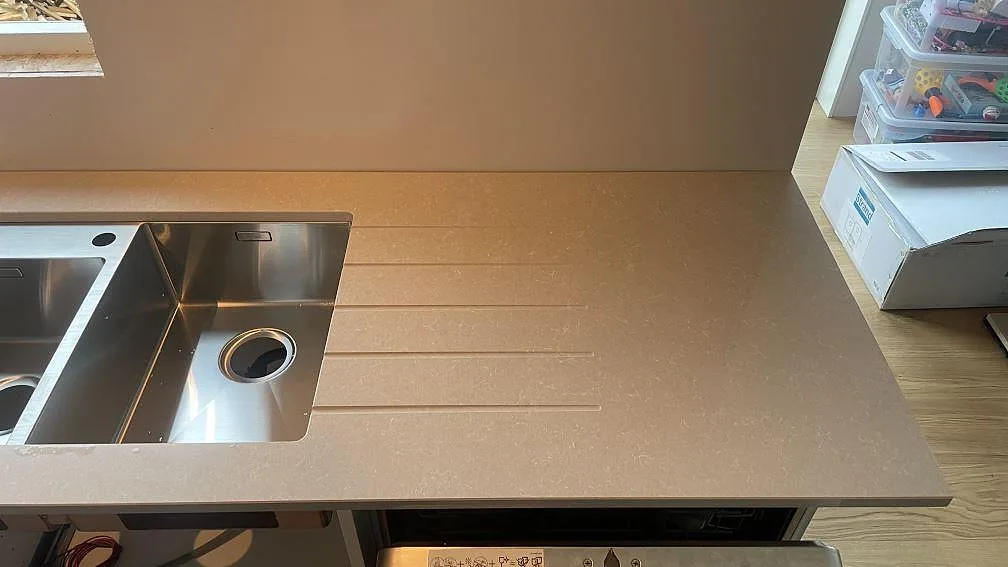 Detalj av polerad Technistone Noble Ivory White som köksbänk med rostfri diskho, avställningsyta och spårad avrinningsyta i Göteborg.