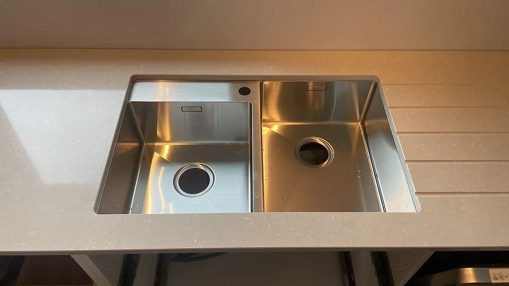 Rostfri dubbelho i en polerad köksbänkskiva av Technistone Noble Ivory White, monterad mot vägg i Göteborg.