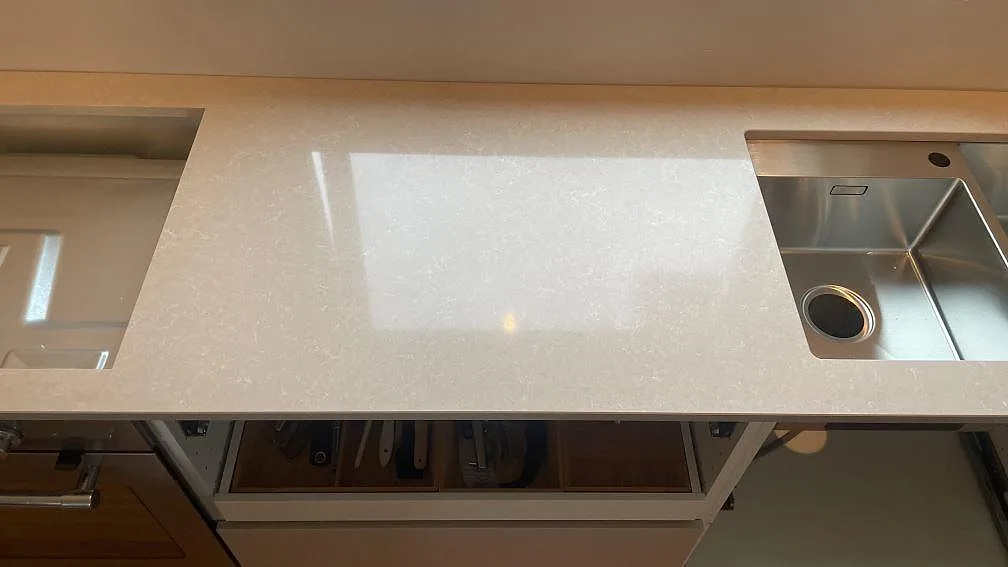 Närbild på polerad Technistone Noble Ivory White med fönsterreflex och rostfri diskho i ett kök i Göteborg.