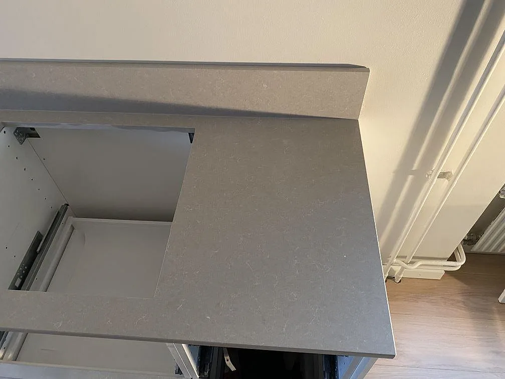 Högerände av köksbänkskiva i Technistone Noble Ivory White med hällurtag, uppvikt stänkkant och öppen stomme i Helsingborg.
