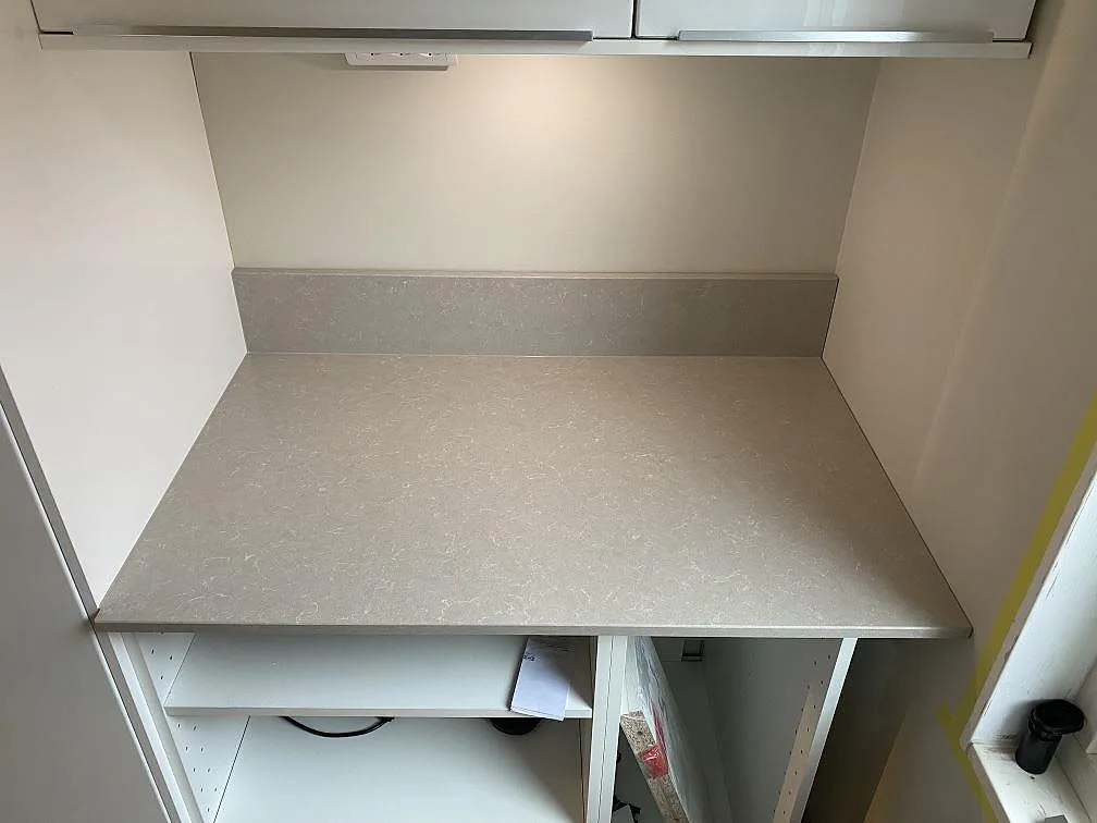 Rak köksbänk i polerad Technistone Noble Ivory White med uppvikt stänkkant och ljusa köksstommar under montering i Helsingborg.