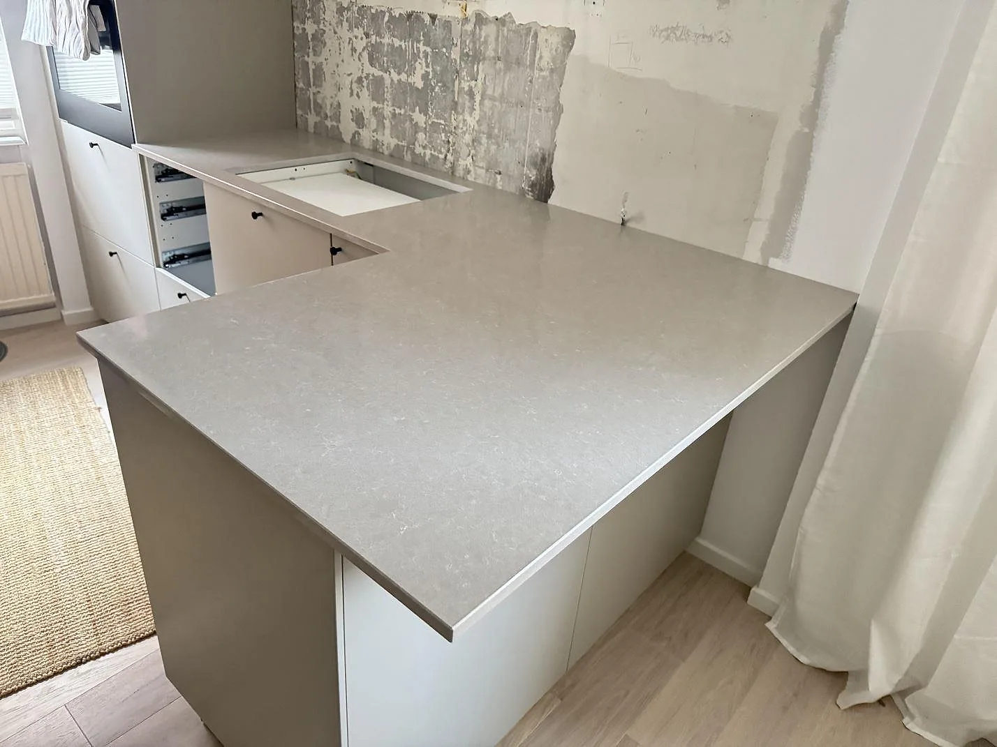 Köksbänkskiva i Technistone Noble Ivory White, polerad ljus kvartskomposit, med halvö och väggbänk i ett kök under montering i Helsingborg.