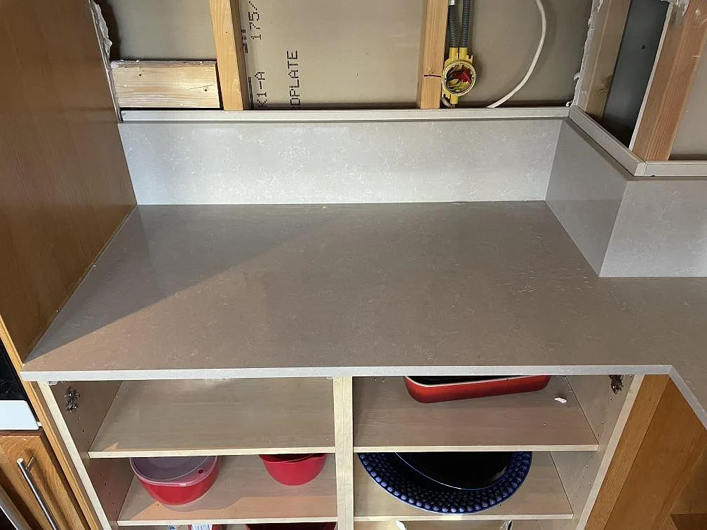 Vänster del av polerad Technistone Noble Ivory White köksbänkskiva i komposit med låg stänkkant och öppen träinredning i Hisings kärra.