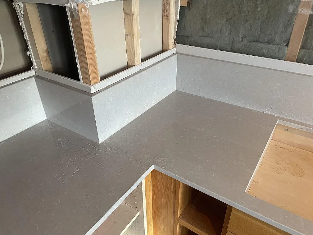 Hörnsektion i polerad Technistone Noble Ivory White komposit med uppvikt stänkkant och hällurtag i ett kök i Hisings kärra.