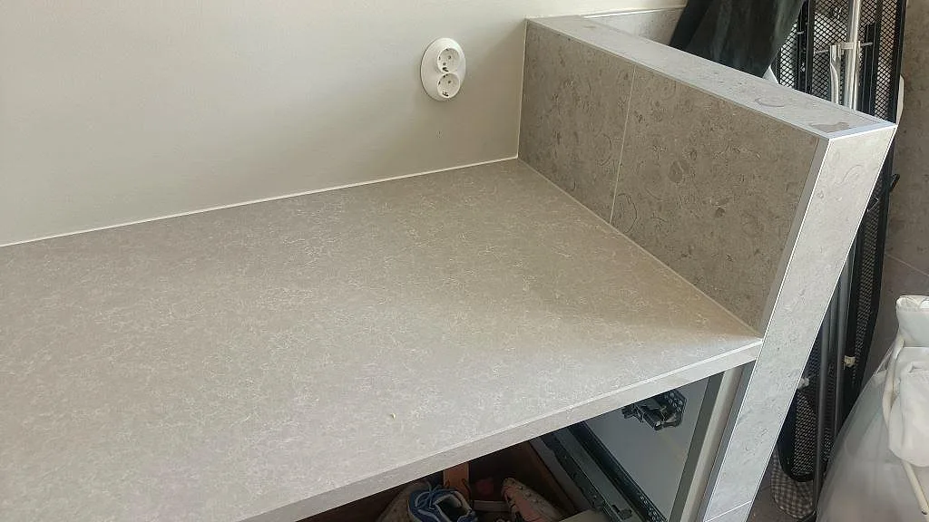Stänkkant i Technistone Noble Ivory White som viker upp mot väggen, med synlig ådring i den gråbeige kompositen i ett kök i Höllviken.
