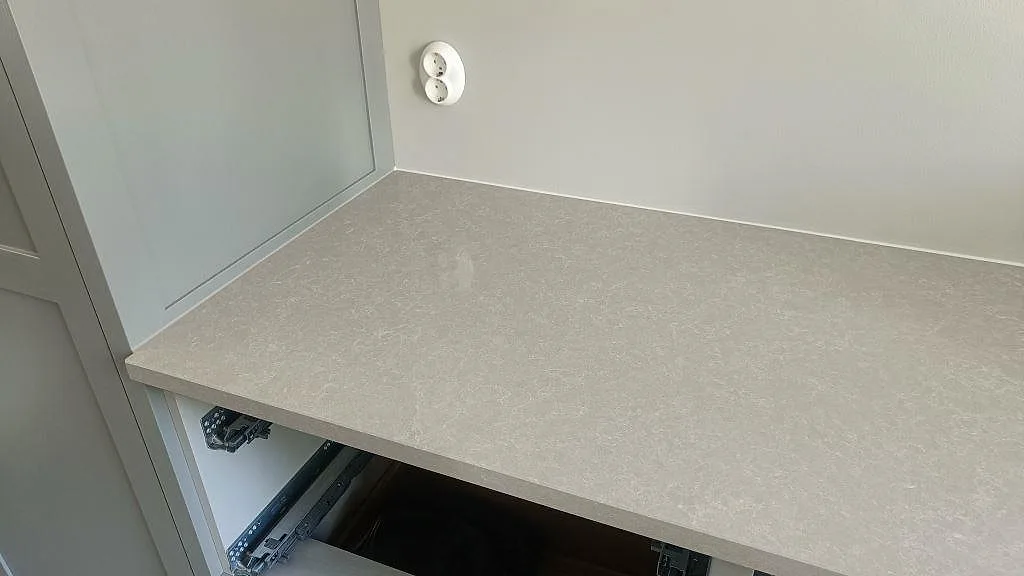 Ovanljus topp av bänkskiva i Technistone Noble Ivory White, ljus gråbeige kvartskomposit, i ett kök under montering i Höllviken.