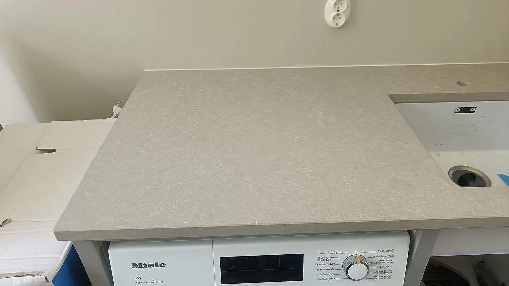 Bänkskiva i Technistone Noble Ivory White över tvättmaskin i tvättstugan, ljus gråbeige komposit i Höllviken.