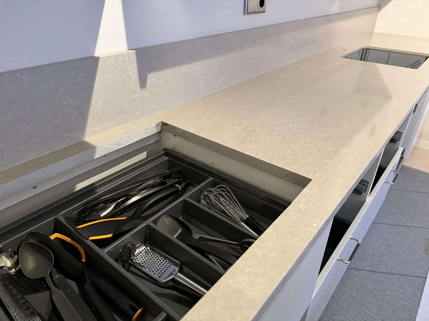 Lång köksbänkskiva i polerad Technistone Noble Ivory White med besticklåda, diskho och stänkkant i Höllviken.