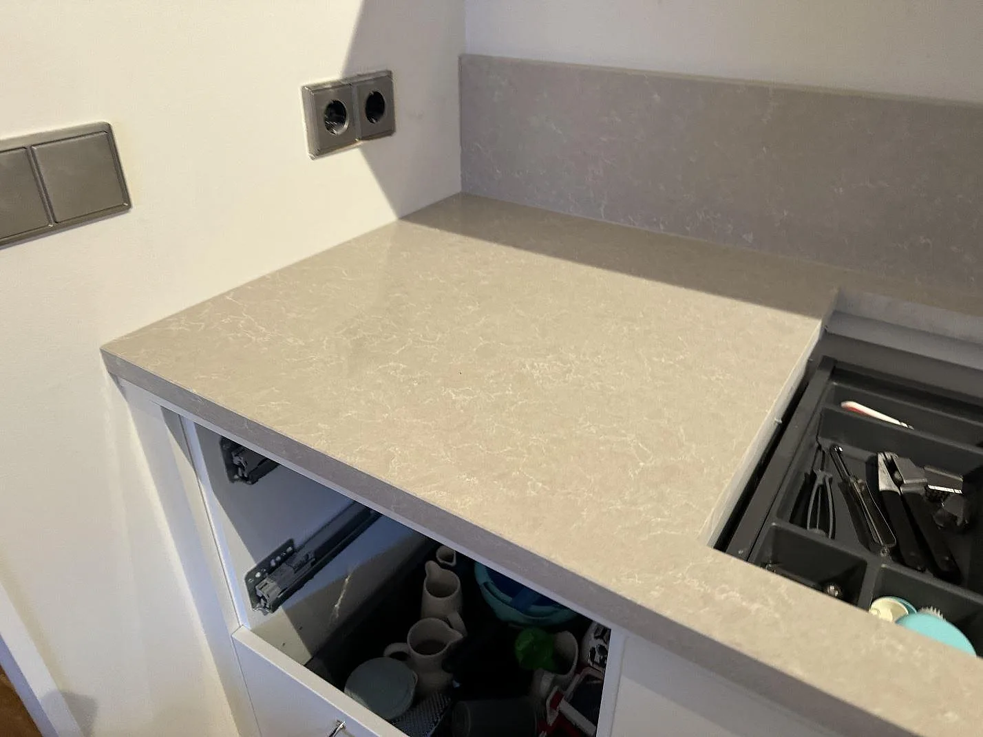 Hörn av köksbänkskiva i polerad Technistone Noble Ivory White med uppvikt stänkkant och öppna lådor i Höllviken.