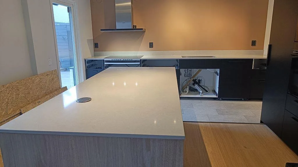 Köksbänkskiva i polerad Technistone Noble Ivory White med stor köksö, häll och diskhozon i ett kök i Höllviken.