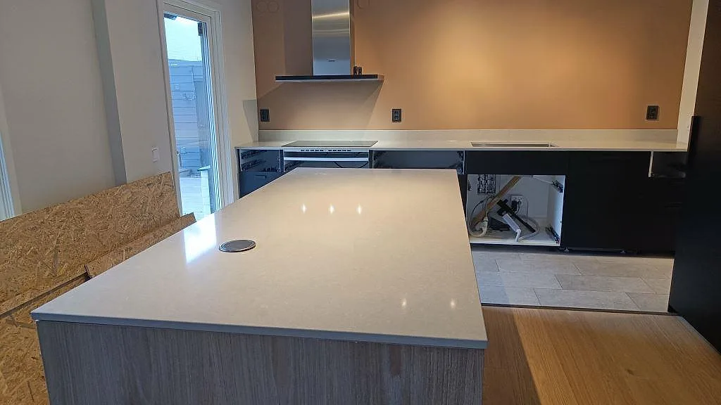 Polerad kvartskomposit i Technistone Noble Ivory White på köksö och väggbänk under montering i Höllviken.