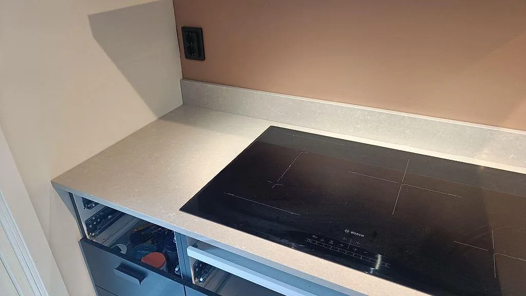 Närbild på väggbänk i Technistone Noble Ivory White, polerad, med svart spishäll och låg stänkkant i Höllviken.