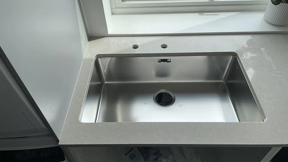 Närbild på polerad Technistone Noble Ivory White komposit med rostfri diskho och blandarhål i tvättstugan i Hørsholm.