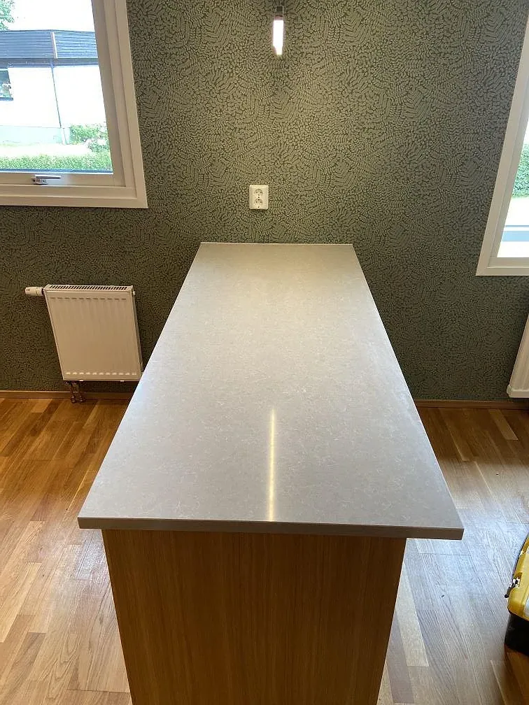 Polerad köksö i ljus elfenbensvit Technistone Noble Ivory White mot en grön accentvägg, fotograferad under montering i ett kök i Horred.