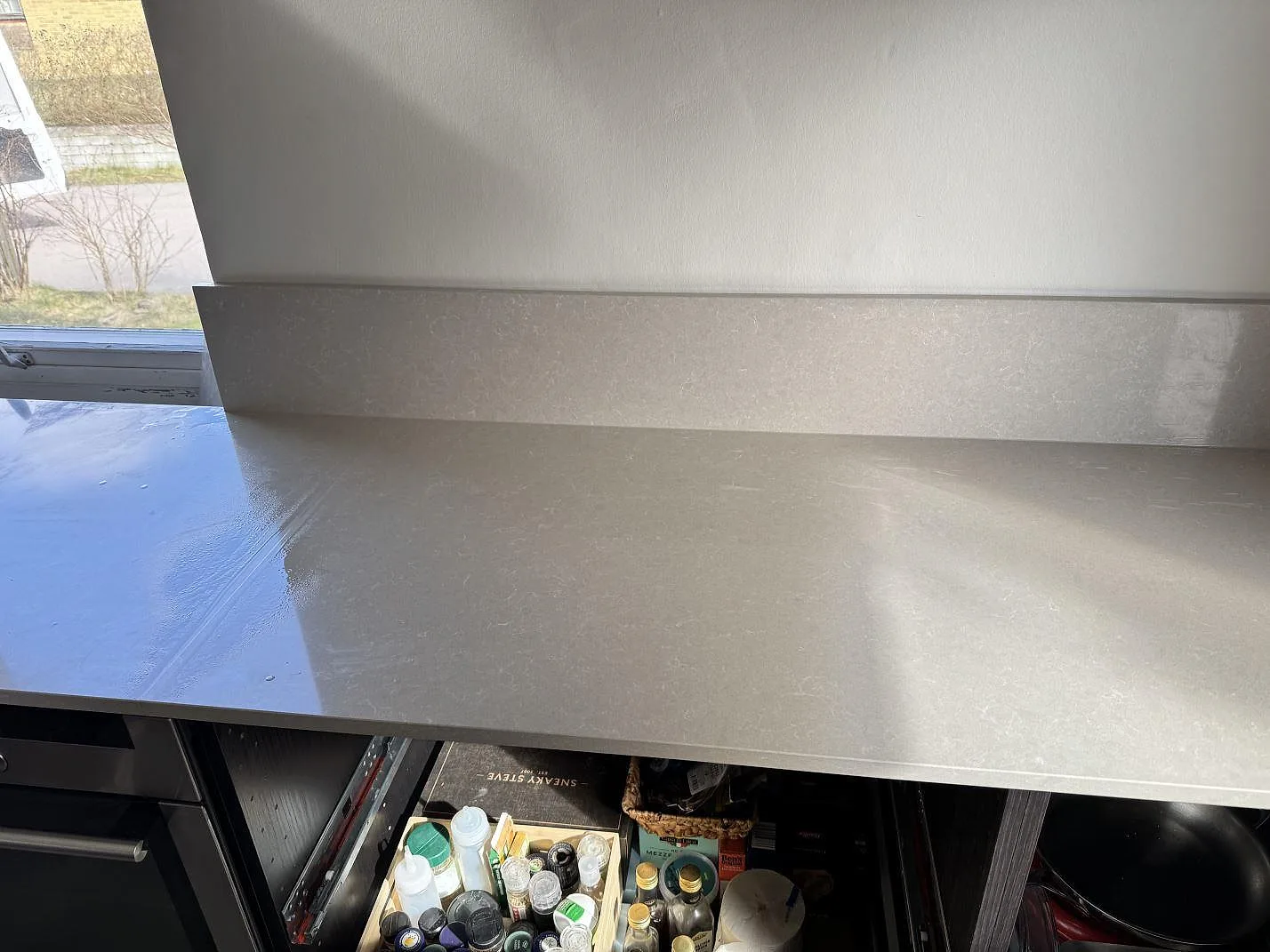 Lång bänkrad i polerad Technistone Noble Ivory White, kvartskomposit, med låg stänkkant och öppna köksstommar i Hovås.