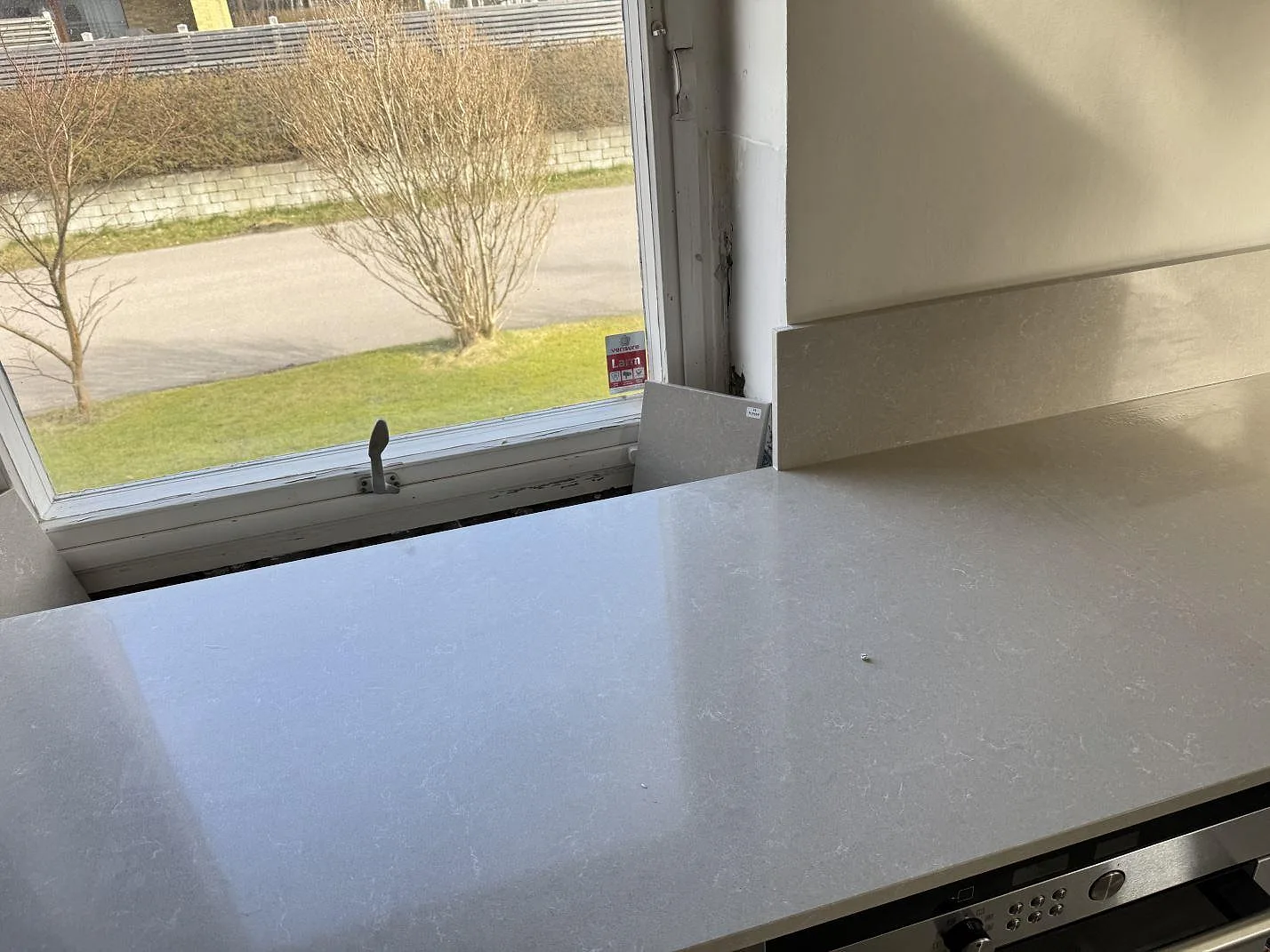 Polerad köksbänkskiva i Technistone Noble Ivory White, kvartskomposit, vid fönster med stänkkant och ugnsfront i Hovås.