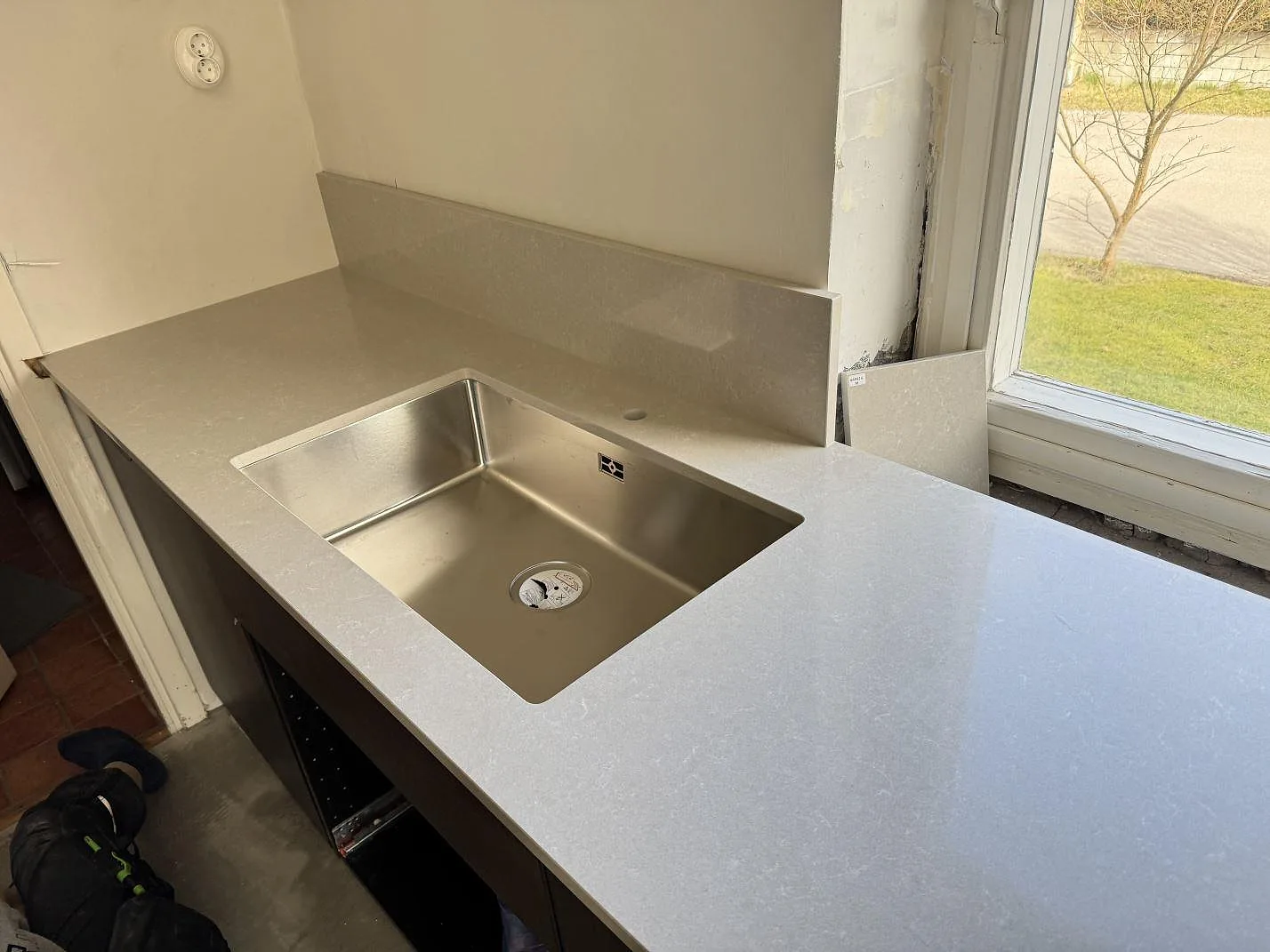 Polerad köksbänkskiva i Technistone Noble Ivory White, kvartskomposit, med rostfri diskho och stänkkant vid fönster i Hovås.