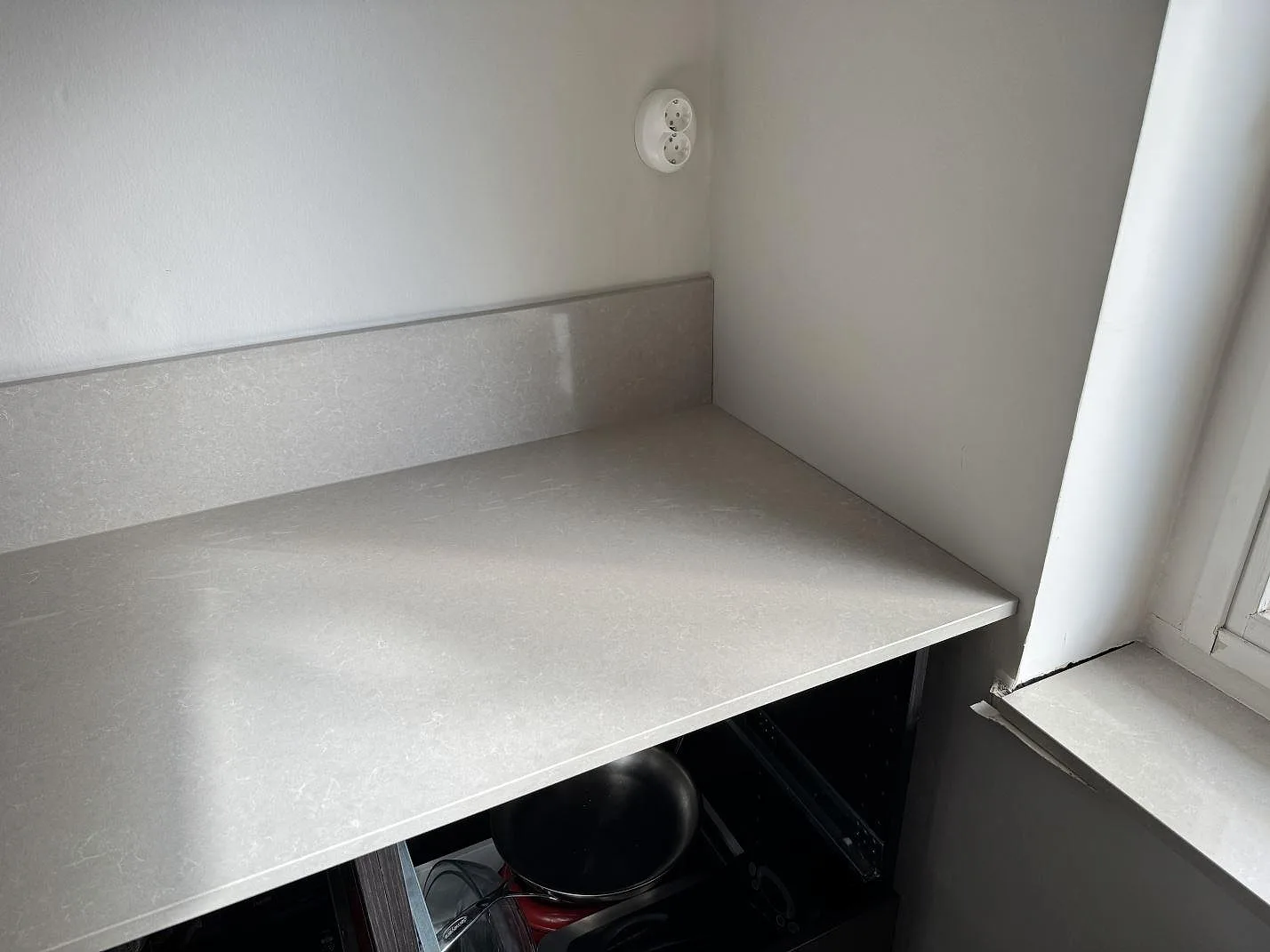 Hörn av köksbänkskiva i polerad Technistone Noble Ivory White, kvartskomposit, med stänkkant och fönsterljus i Hovås.