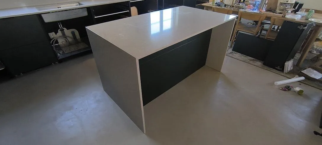 Köksö med polerad Technistone Noble Ivory White som ljus kompositskiva i ett kök under montering i Huddinge.