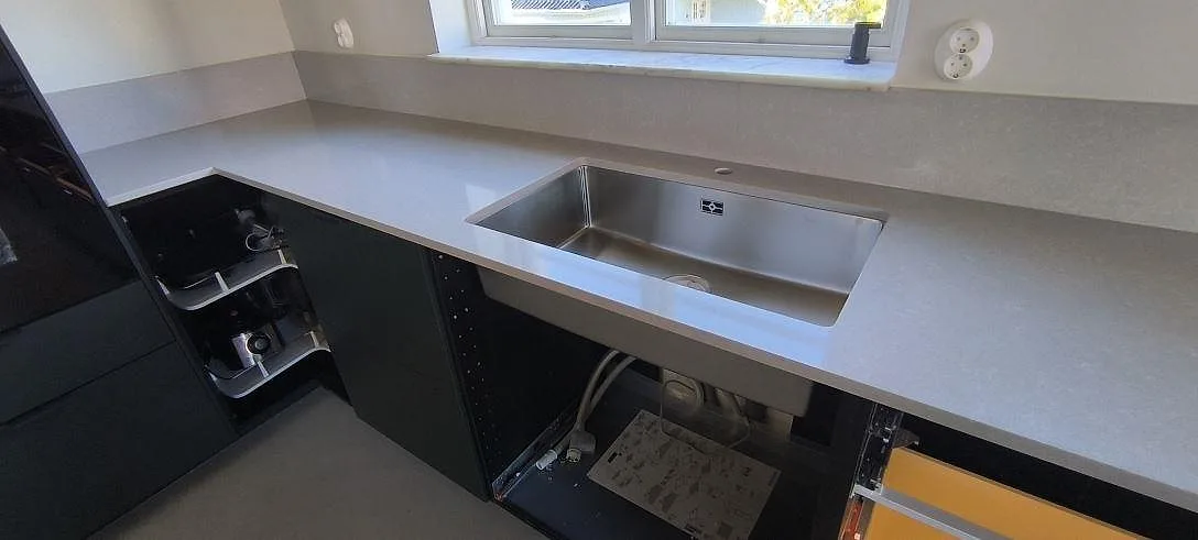 Polerad köksbänkskiva i Technistone Noble Ivory White med rostfri diskho och uppvikt stänkkant i ett kök i Huddinge.