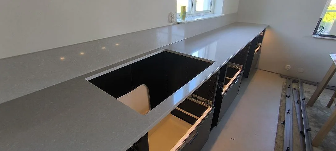 Detalj av polerad Technistone Noble Ivory White med hällurtag, stänkkant och öppna köksstommar under montering i Huddinge.