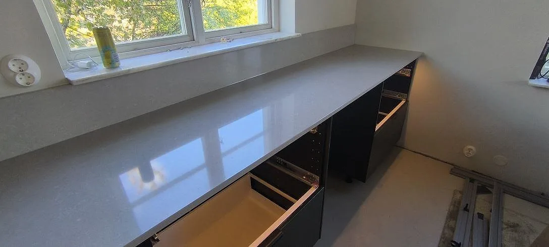 Polerad bänkskiva i Technistone Noble Ivory White längs fönstervägg med stänkkant och öppna stommar i Huddinge.