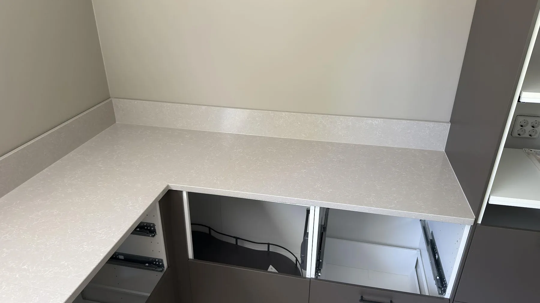 Hörnparti av köksbänk i vit Technistone Noble Ivory White med fint spräcklig struktur och uppvikt stänkkant, polerad kvartskomposit, i ett kök i Ingarö.