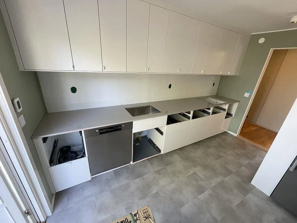 Översikt av kök under montering i Järfälla med polerad bänkskiva i Technistone Noble Ivory White komposit längs väggen och vita skåp.