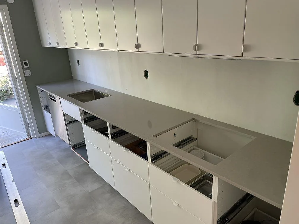 Köksbänkskiva i polerad Technistone Noble Ivory White komposit, monterad som rak bänkrad med öppna köksstommar och urtag i Järfälla.