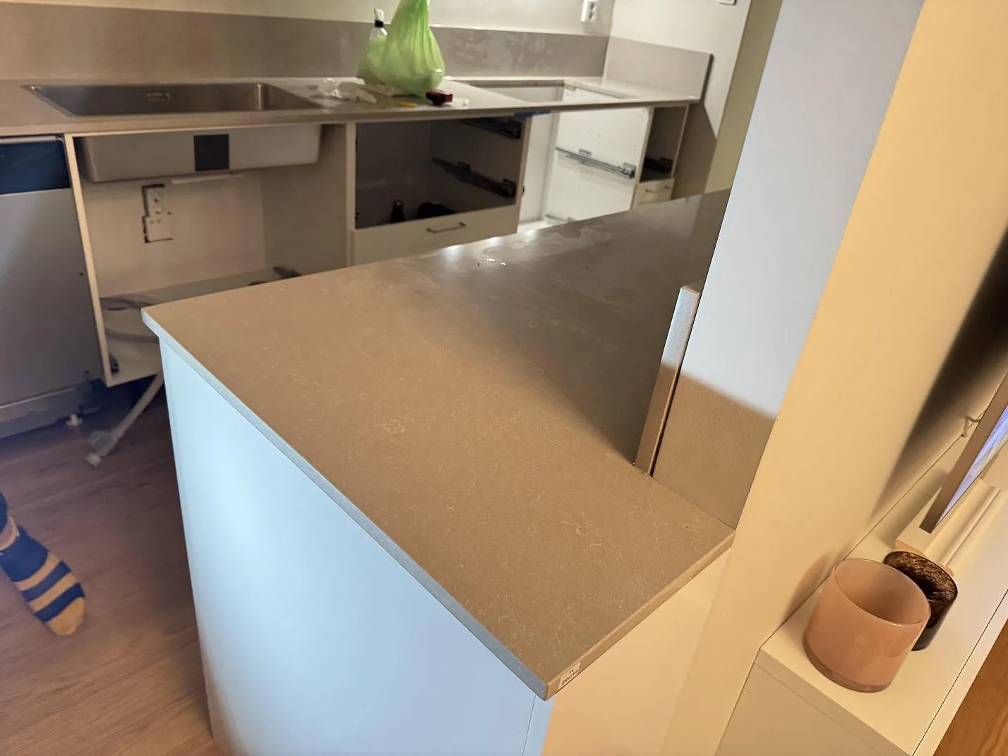 Översikt av kök i Jönköping med polerad bänkskiva i Technistone Noble Ivory White, uppvikt stänkkant, rostfri diskho och öppna stommar under montering.