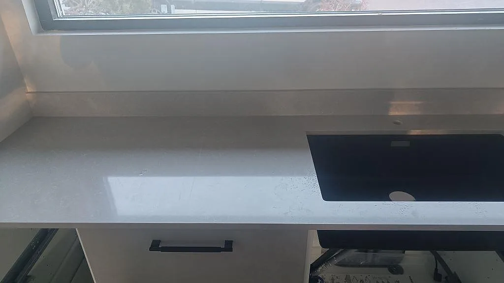 Polerad Technistone Noble Ivory White köksbänkskiva med svart diskho och stänkskydd under fönster i Kalmar.