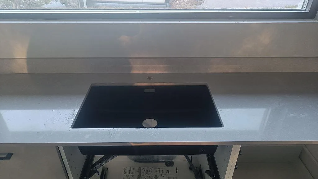 Närbild på köksbänkskiva i polerad Technistone Noble Ivory White med svart diskho under fönster i Kalmar.