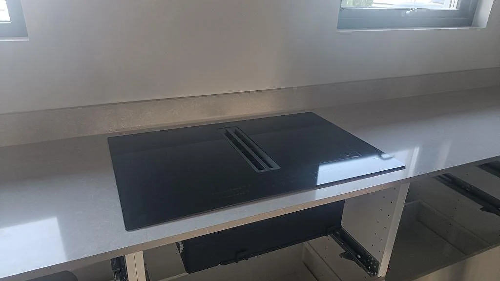 Detalj av polerad kompositbänkskiva i Technistone Noble Ivory White med svart häll och ljus stänkkant i kök i Kalmar.