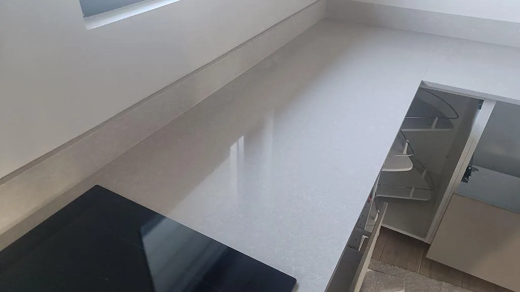 L-formad köksbänkskiva i polerad Technistone Noble Ivory White med ljus ådring, stänkkant och häll i Kalmar.