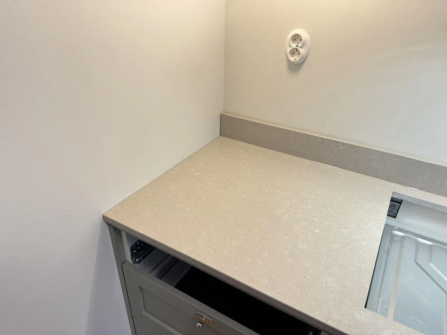 Hörnsektion av köksbänkskiva i vit Technistone Noble Ivory White i Kalmar med vägguttag och uppvikt stänkkant i polerad kvartskomposit.