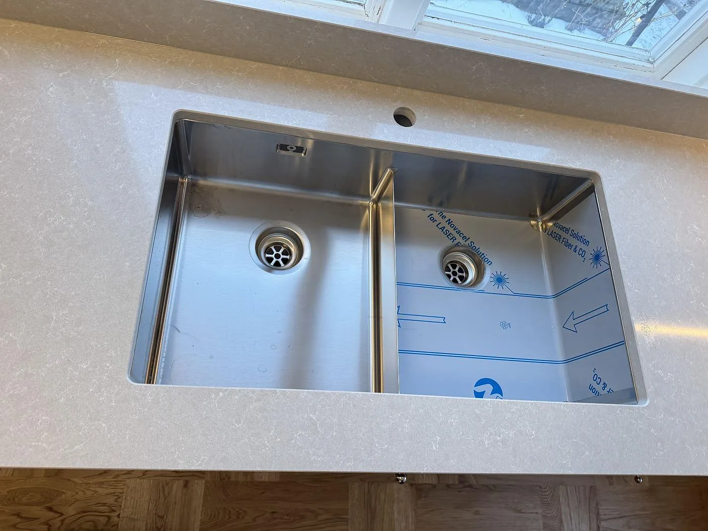 Underlimmad rostfri dubbelho infälld i vit köksbänkskiva i Technistone Noble Ivory White i ett kök i Kalmar, sett uppifrån.