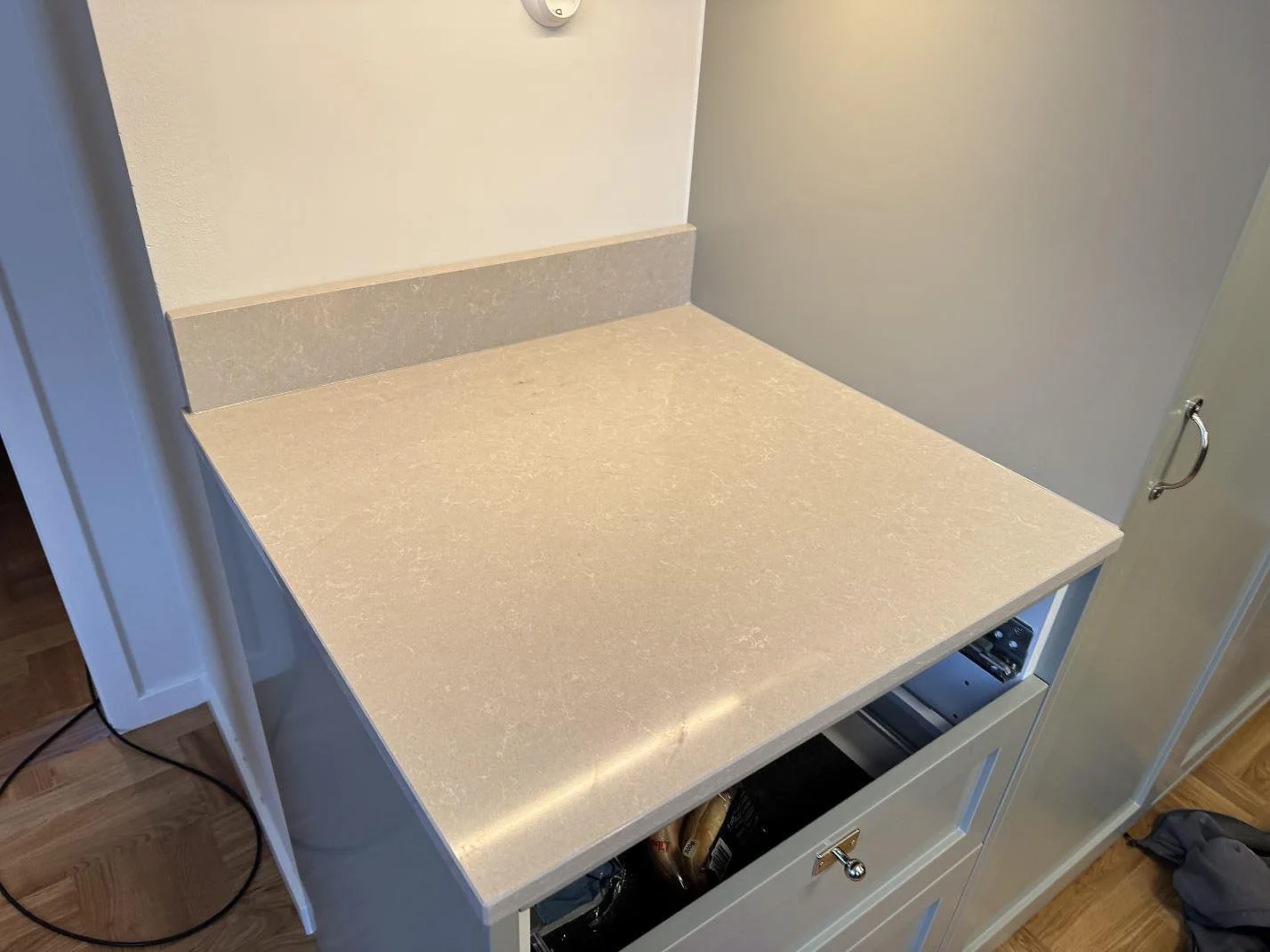 Bänkskiva i Technistone Noble Ivory White i Kalmar med uppvikt stänkkant i samma sten ovanför en öppen köksstomme under montering.
