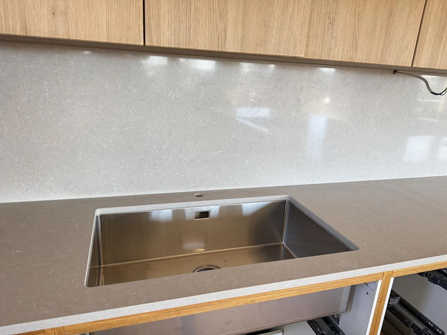 Köksbänkskiva i polerad Technistone Noble Ivory White komposit med underlimmad rostfri diskho och stänkskydd under överskåp i Karlshamn.