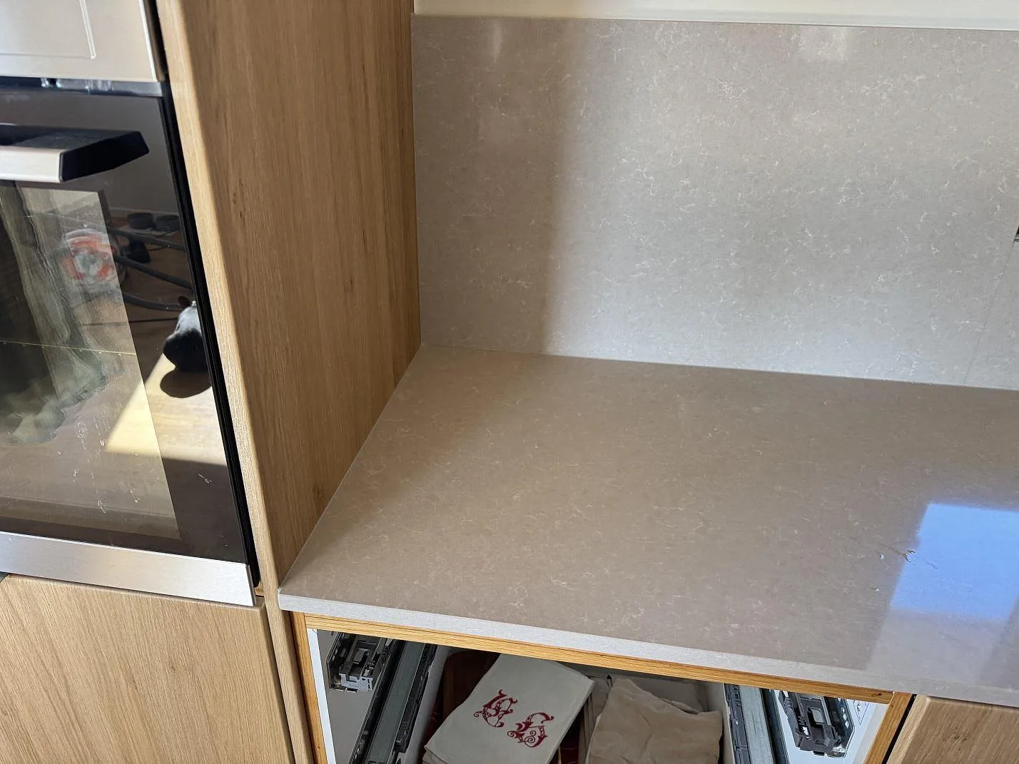 Sidovy av polerad köksbänkskiva i Technistone Noble Ivory White komposit intill ugn och trästomme i Karlshamn.