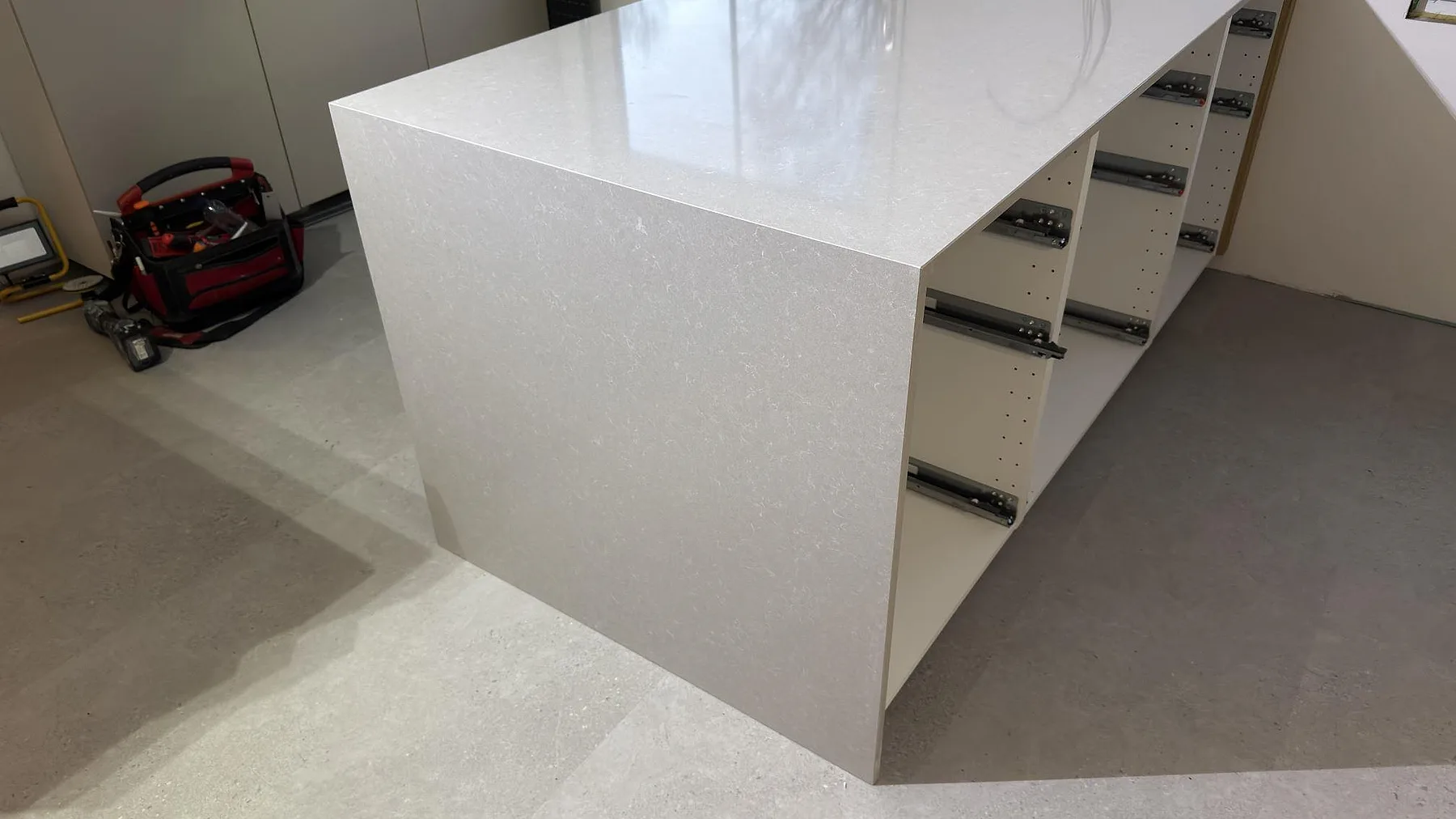 Detalj av köksö i Technistone Noble Ivory White med ljus polerad kvartskomposityta och öppna stommar under montering i Karlskoga.
