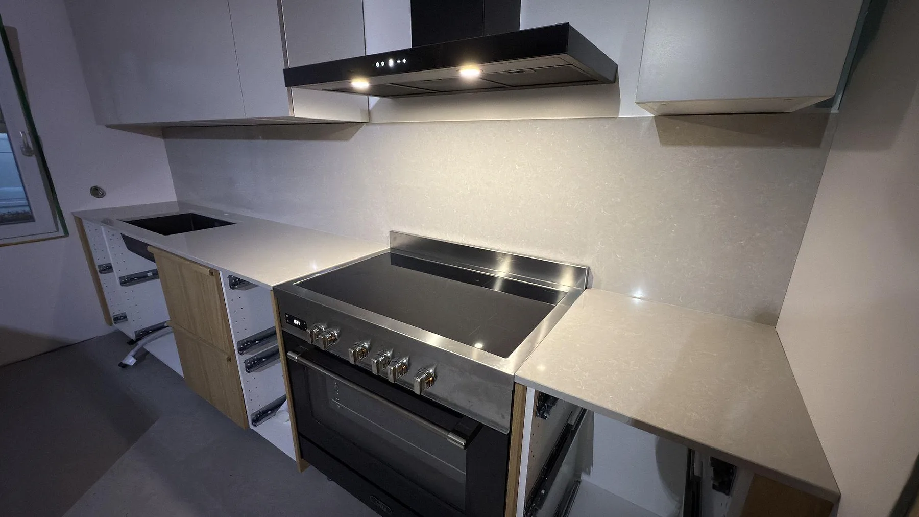 Polerad köksbänkskiva och stänkskydd i Technistone Noble Ivory White bakom spisen i ett kök i Karlskoga.