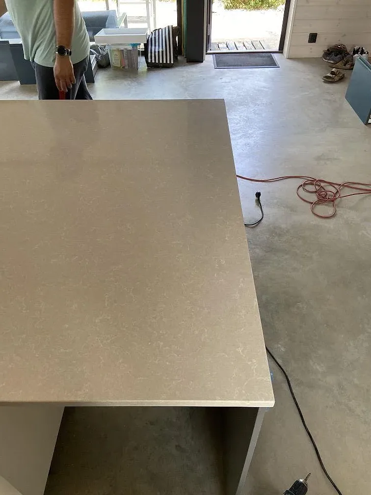Köksö i ljus Technistone Noble Ivory White kvartskomposit med rostfri diskho, sedd från sidan under montering i ett kök i Kivik.