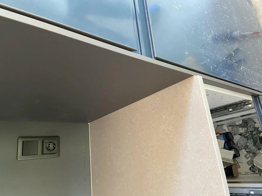 Detalj av bänkskiva och uppvikt stänkkant i Technistone Noble Ivory White vid fönstret i ett kök i Kivik.